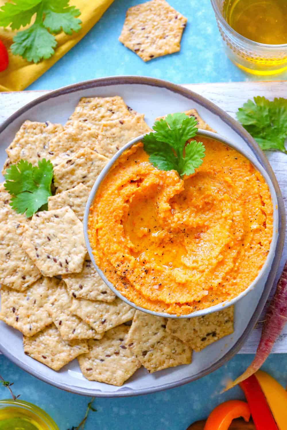 A bowl of troasted vegetable dip with crackers on a round plate