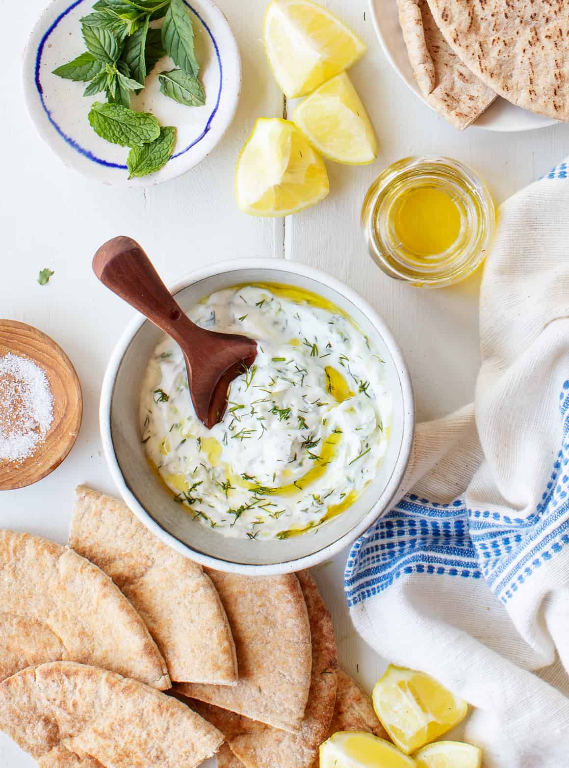 A bowl of tzatziki and pitta, small bowl with olive oil and lemon slices on a table